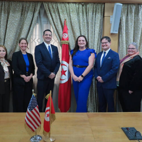 A picture showing a group of College of Computing officials including Dean Marouane Kessentini pose for a  photo. Between them is a Tunisian flag. A table in front them has the USA and Tunisia Flag